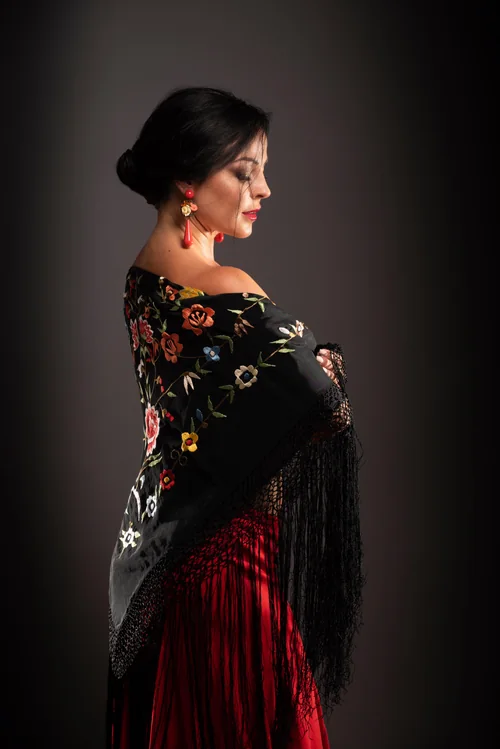 Veronica Pavon in profile, draped in a black embroidered shawl over a red skirt.